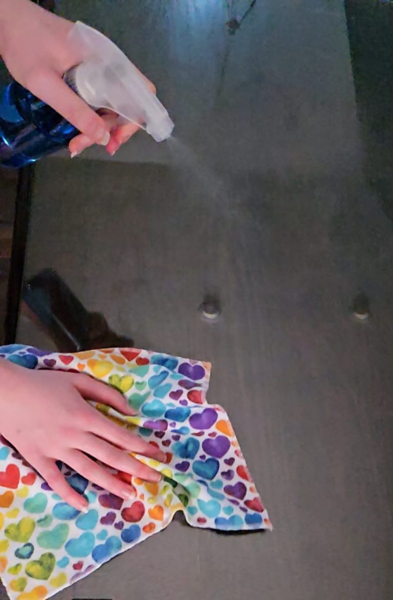 Picture shows rainbow heart cloth being used to clean a glass surface Person spraying a colorful cloth on a surface for cleaning.
